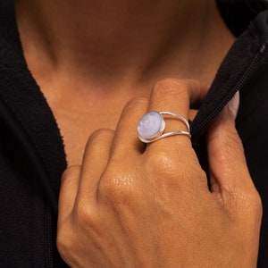 May include: A silver ring with a light purple gemstone set in a bezel setting. The ring has a double band design.