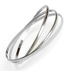 May include: A set of three silver bangle bracelets, each with a slightly different width, intertwined together. The bracelets are marked with "925", indicating they are made of sterling silver.