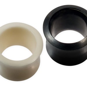 Könnte beinhalten: Zwei Ohrdehner, einer schwarz und einer weiß. Die Dehnungen sind aus einem glatten, polierten Material gefertigt und haben ein ausgestelltes Design.