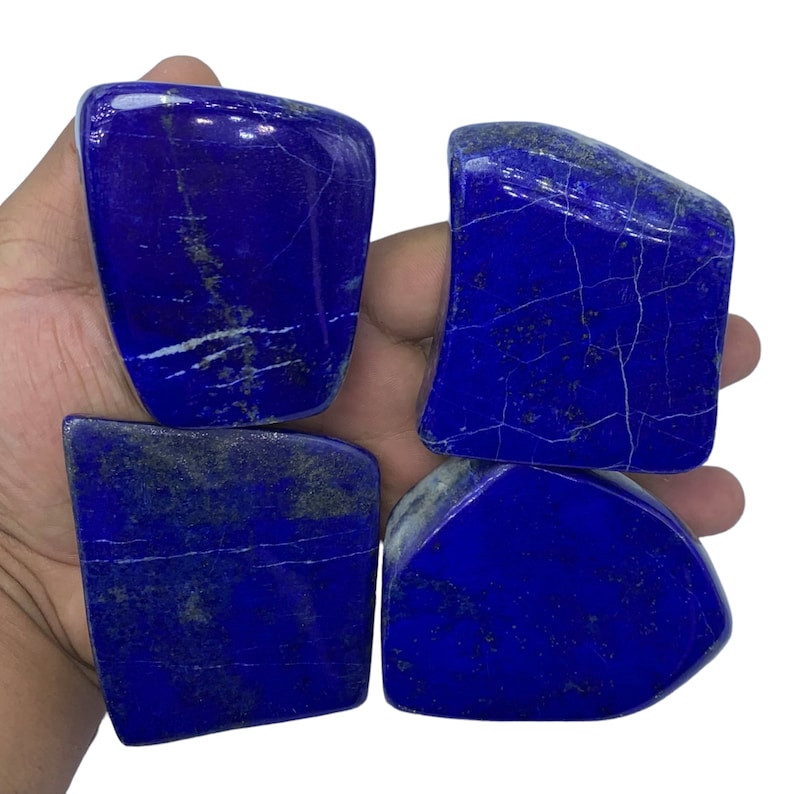 May include: Four smooth, polished, dark blue lapis lazuli stones with white and gold veins. The stones are irregularly shaped and have a natural, rough texture.