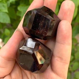 Puede incluir: Dos cristales de granate facetados de color rojo oscuro. Los cristales tienen la forma de un dodecaedro.