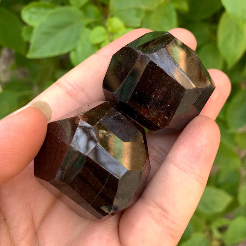 Puede incluir: Dos cristales de piedra preciosa facetados de color marr&oacute;n oscuro. Los cristales tienen forma de pir&aacute;mide con una base plana.