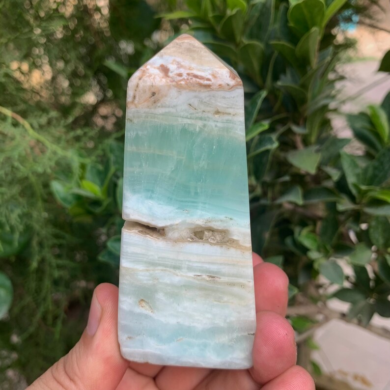 Puede incluir: Una punta de cristal azul claro y blanco, tambi&eacute;n conocida como torre u obelisco, con una punta puntiaguda. El cristal es transl&uacute;cido y tiene una textura natural y rugosa.