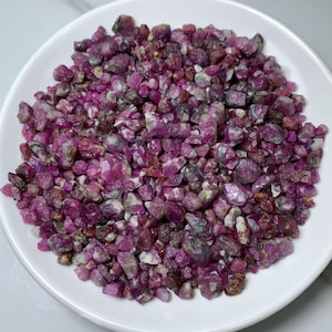 Op de afbeelding: Een close-up van een stapel kleine, roze robijn edelstenen. De robijnen zijn ruw en hebben een natuurlijke, onbewerkte uitstraling.