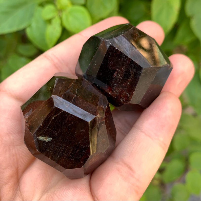 Puede incluir: Dos cristales de granate rojo oscuro facetados. Los cristales tienen la forma de un dodecaedro.