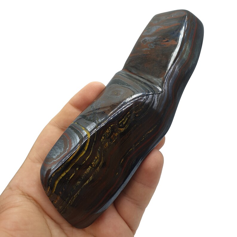 以下が含まれることがあります： 金色と銀色の筋が入った、大きく滑らかな濃い茶色と黒の縞模様のタイガーアイストーン。石は長く、平らで丸みを帯びた長方形の形をしています。