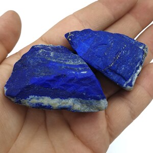 May include: Two rough, natural pieces of lapis lazuli, a deep blue gemstone with flecks of gold pyrite. The stones are irregular in shape and have a rough, unpolished texture.