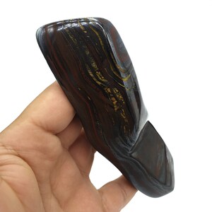 以下が含まれることがあります： 滑らかで磨かれた、濃い茶色、赤、金色のタイガーアイストーン。ユニークな層状のパターンが特徴です。石は、丸みを帯びた角を持つ、長く狭い長方形の形をしています。