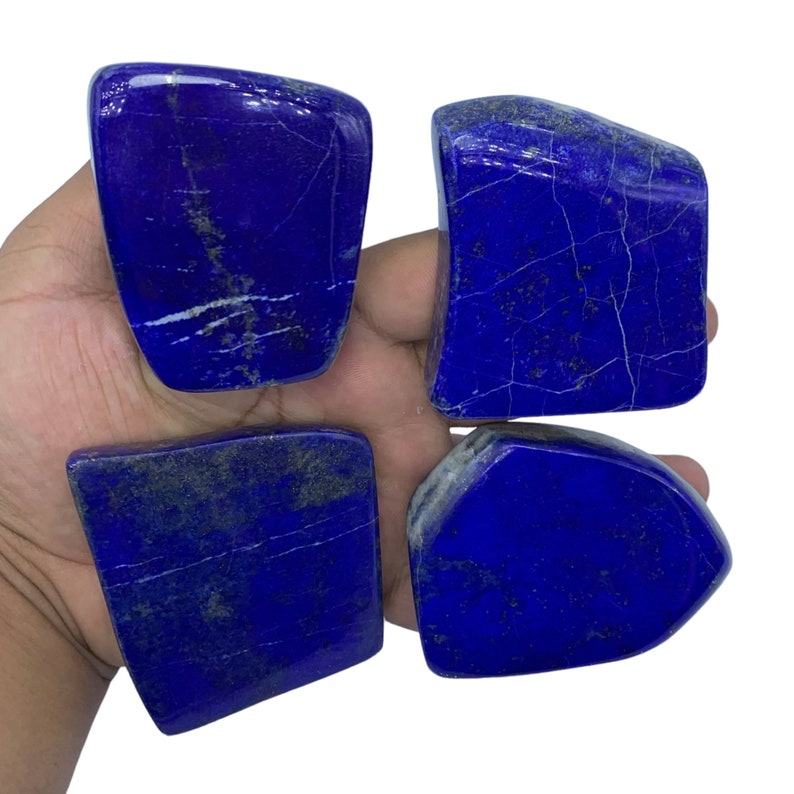 May include: Four rough-cut, dark blue Lapis Lazuli stones with white veins and gold flecks. The stones are arranged in a square shape.