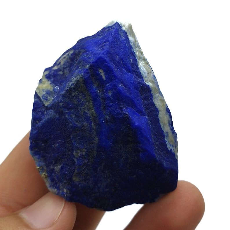 May include: A large, rough, blue lapis lazuli stone with white and gold veins. The stone is being held in a hand.