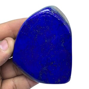 May include: A large, deep blue, polished lapis lazuli stone with gold flecks. The stone is irregularly shaped and has a smooth, polished surface.