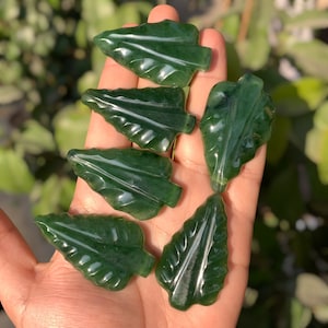 Könnte beinhalten: Sechs grüne Jade-Anhänger in Blattform mit einem geschnitzten Design. Die Anhänger sind glatt und poliert.