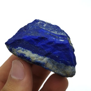 May include: A rough, dark blue lapis lazuli stone with white and gold veins. The stone is a natural mineral and has a rough, uneven surface.