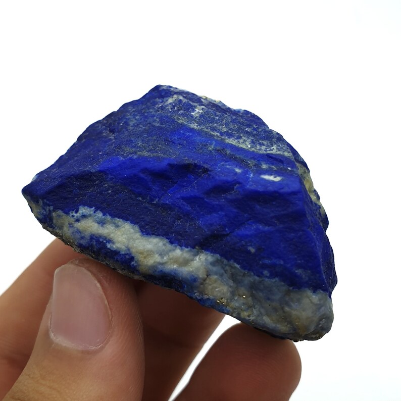 May include: A rough, dark blue lapis lazuli stone with white and gold veins. The stone is a natural mineral and has a rough, uneven surface.