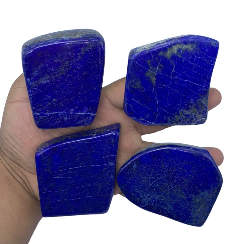 May include: Four pieces of raw, rough-cut lapis lazuli. The stones are a deep blue with white veins and flecks of gold pyrite.