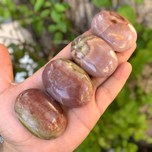 May include: Four smooth, polished, oval-shaped stones with a pink, white, and brown colour pattern. The stones are arranged in a row, with the largest stone at the top and the smallest stone at the bottom.