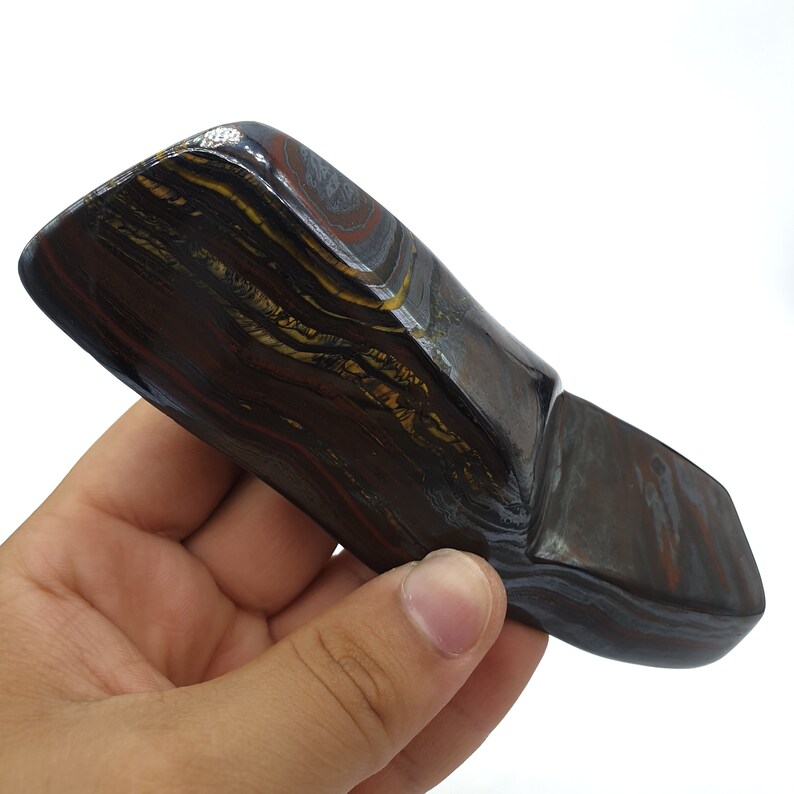 以下が含まれることがあります： 金色と赤色の縞模様が入った、滑らかな濃い茶色と黒色の石。石は細長い平らな楕円形です。