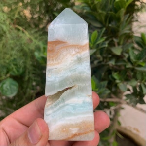 Puede incluir: Una punta de cristal obelisco con bandas azul claro y marr&oacute;n. El cristal tiene una grieta natural que lo atraviesa.