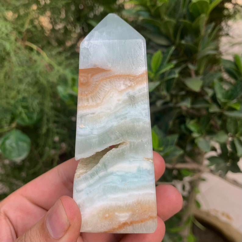 Puede incluir: Una punta de cristal obelisco con bandas azul claro y marr&oacute;n. El cristal tiene una grieta natural que lo atraviesa.