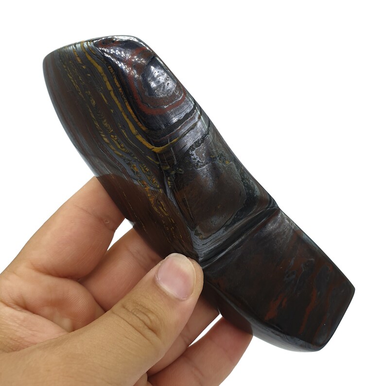 以下が含まれることがあります： 独特な湾曲した形をした、滑らかな濃い茶色と金のタイガーアイストーン。石は、茶色、金色、黒色の色合いの層状の縞模様をしています。