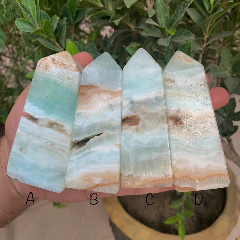 Puede incluir: Cuatro puntas de cristal de &aacute;gata azul y blanco con bandas, etiquetadas como A, B, C y D. Las puntas est&aacute;n dispuestas en fila, con las puntas apuntando hacia la derecha. Las puntas son lisas y pulidas, y las bandas son muy distintas.