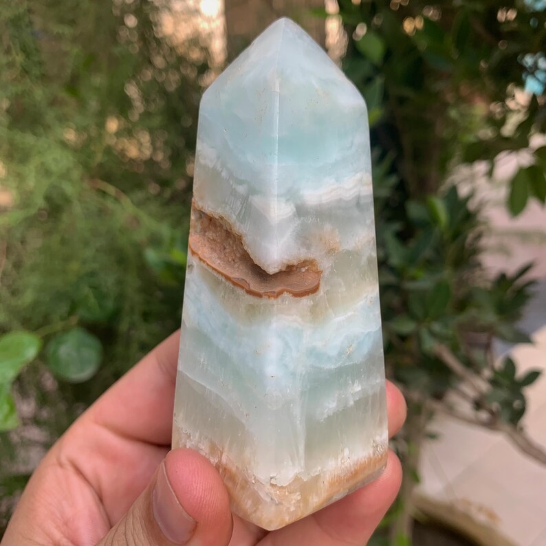 Puede incluir: Una punta de cristal azul claro y marr&oacute;n, tambi&eacute;n conocida como torre de cristal, con una parte superior puntiaguda y una base plana. El cristal tiene un aspecto en capas con bandas blancas y marrones.