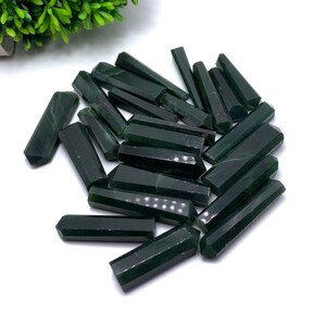 May include: A pile of dark green jade crystal points, also known as wands or sticks. The points are smooth and polished, with a slightly translucent appearance.