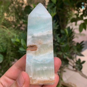 Puede incluir: Una punta de cristal azul claro y marr&oacute;n, tambi&eacute;n conocida como obelisco de cristal, es una piedra natural con una parte superior puntiaguda y una base plana.