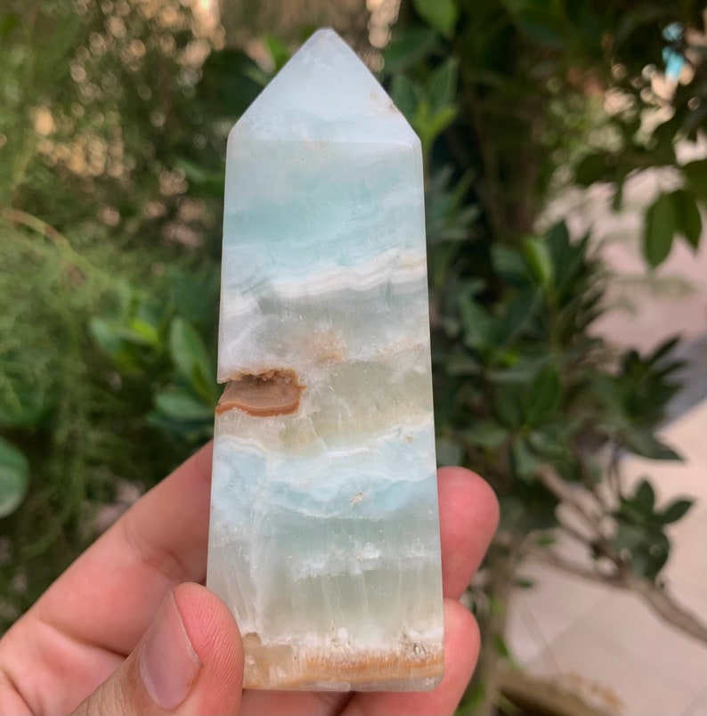 Puede incluir: Una punta de cristal azul claro y marr&oacute;n, tambi&eacute;n conocida como obelisco de cristal, es una piedra natural con una parte superior puntiaguda y una base plana.