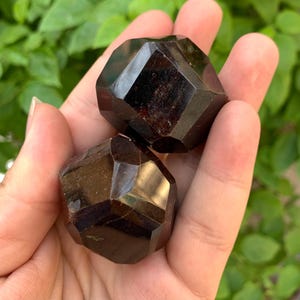 Puede incluir: Dos cristales de granate facetados de color rojo oscuro. Los cristales son lisos y pulidos.