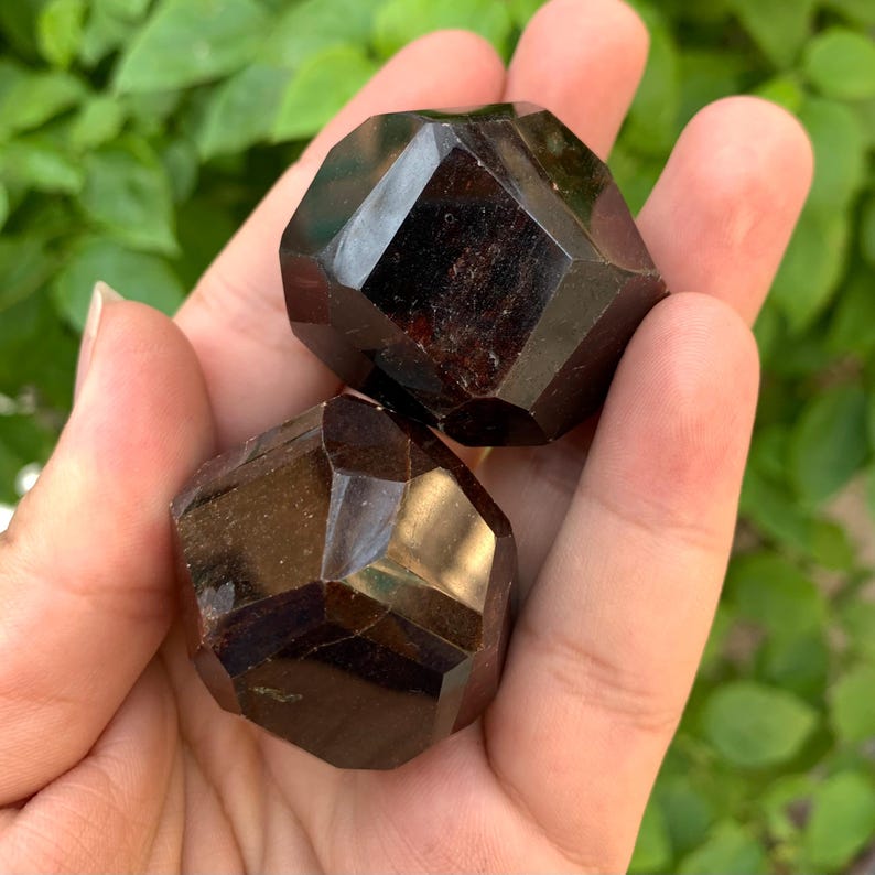 Puede incluir: Dos cristales de granate facetados de color rojo oscuro. Los cristales son lisos y pulidos.