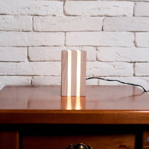 May include: A wooden table lamp with a light wood finish and three white LED lights. The lamp is sitting on a wooden table.