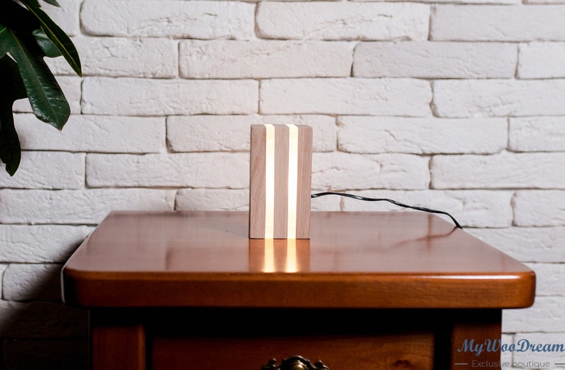May include: A wooden table lamp with a light wood finish and three white LED lights. The lamp is sitting on a wooden table.