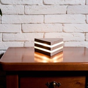 May include: A wooden triangular lamp with two white LED lights inside. The lamp is sitting on a wooden table.