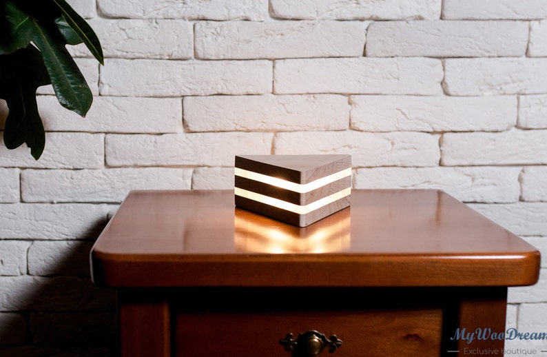 May include: A wooden triangular lamp with two white LED lights inside. The lamp is sitting on a wooden table.