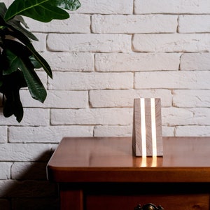 May include: A wooden lamp with a white finish and two thin, white LED lights. The lamp is sitting on a wooden table in front of a white brick wall.