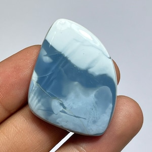 May include: A blue and white opal cabochon with a unique pattern. The stone is cut in a teardrop shape and has a smooth, polished finish.