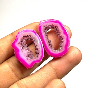 May include: Two halves of a pink agate geode with a hollow center. The geode is translucent and has a white and purple crystalline structure.