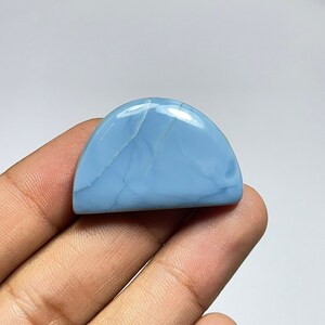 May include: A light blue cabochon opal gemstone with a semi-circular shape and white veins. The opal is smooth and polished.