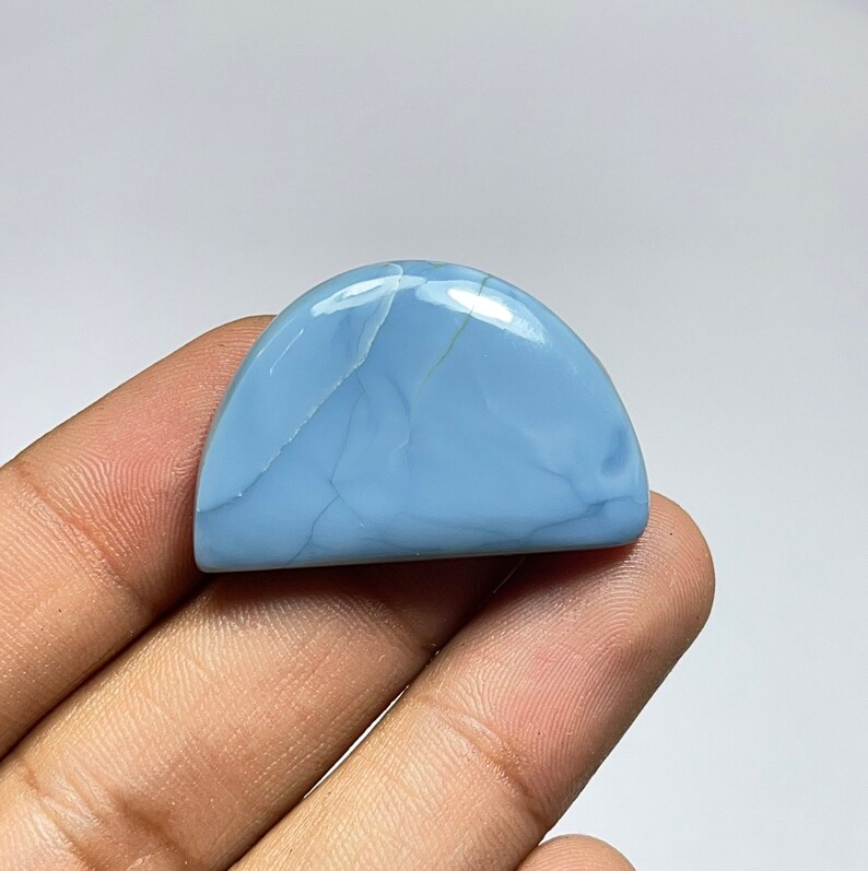May include: A light blue cabochon opal gemstone with a semi-circular shape and white veins. The opal is smooth and polished.