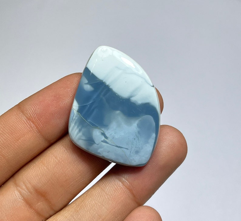 May include: A blue and white opal cabochon with a unique pattern. The stone is cut in a teardrop shape and has a smooth, polished finish.