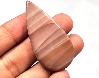 May include: A teardrop-shaped cabochon of banded agate with pink and brown stripes. The stone is translucent and has a smooth, polished surface.