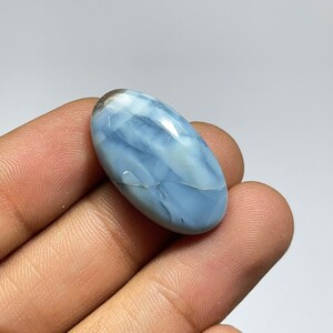 May include: A light blue oval cabochon opal gemstone with white and gray markings. The opal is smooth and polished.