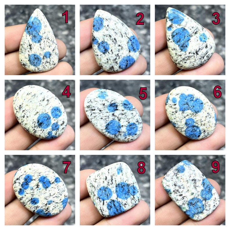 May include: Nine K2 stone cabochons, each with a unique shape and pattern. The stones feature a white base with speckled black and blue spots. The blue spots vary in size and concentration across the cabochons, offering a range of visual textures.