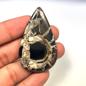 Op de afbeelding: Een traanvormige cabochon van zwart en wit agaat met een draaiende structuur. De agaat heeft een donker centrum en witte aderen die naar buiten stralen.