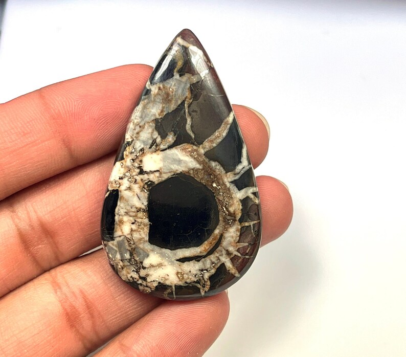 Op de afbeelding: Een traanvormige cabochon van zwart en wit agaat met een draaiende structuur. De agaat heeft een donker centrum en witte aderen die naar buiten stralen.