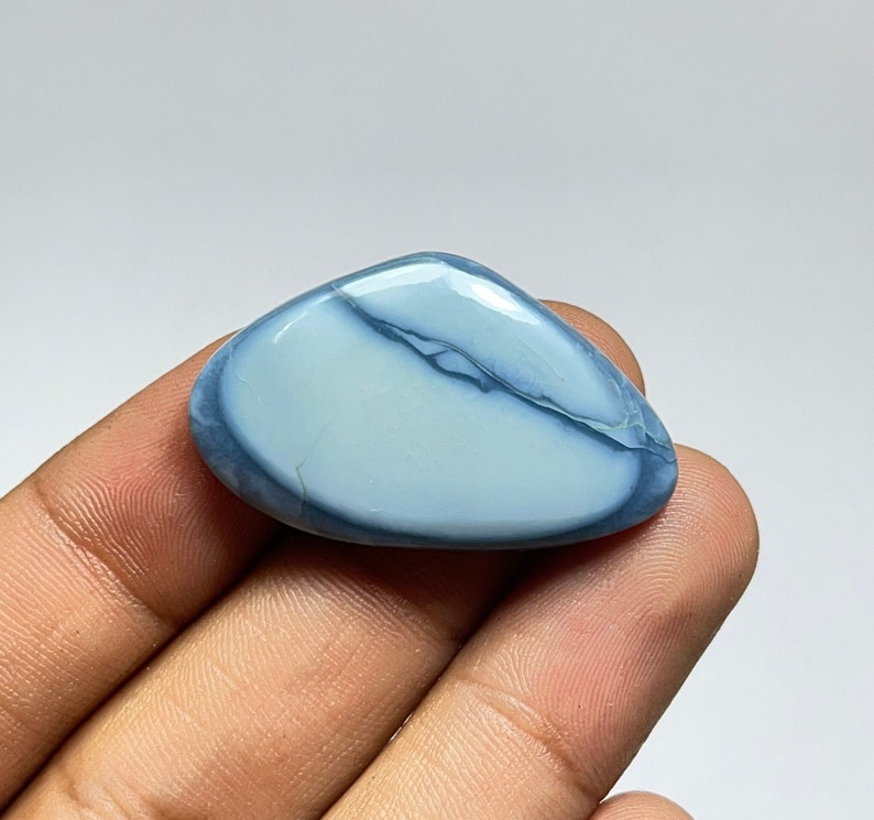 May include: A light blue and white cabochon opal gemstone with a smooth, polished surface. The opal has a unique pattern of white and blue swirls.