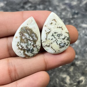 May include: Two teardrop-shaped agate cabochons with a white, brown, and green dendritic pattern. The cabochons are approximately 2 inches long and 1 inch wide.