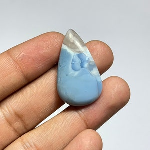 May include: A teardrop-shaped blue opal cabochon with white and gray inclusions. The opal is set in a silver tone setting.