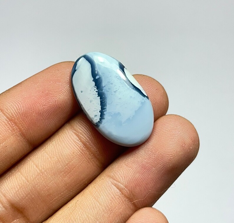 May include: A light blue and white oval cabochon with dark blue veins. The cabochon is a natural stone with a smooth, polished surface.